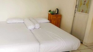A single bed with white bedding in a room with plain walls and a wooden nightstand with a small plant and a kettle. - EXPRESS O 91277 Atiq Homestay Syariah (Serang)