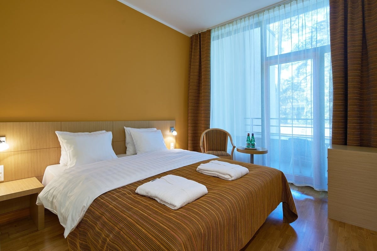 A hotel room with a large bed, a bedside table, a chair, and a small table with bottles.
