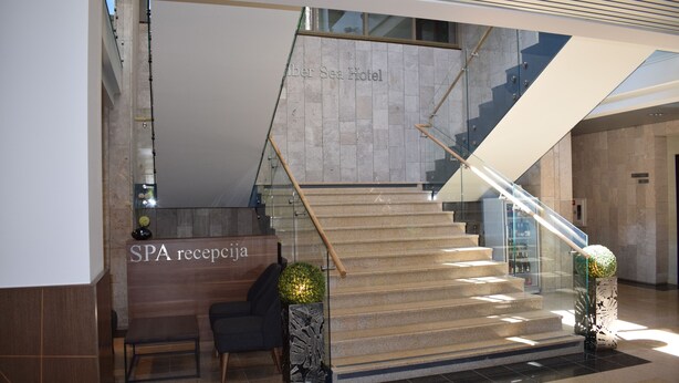 A modern hotel lobby with a reception desk labeled "SPA recepcion" and a staircase leading to upper floors. - Amber Sea Hotel (Jurmala)