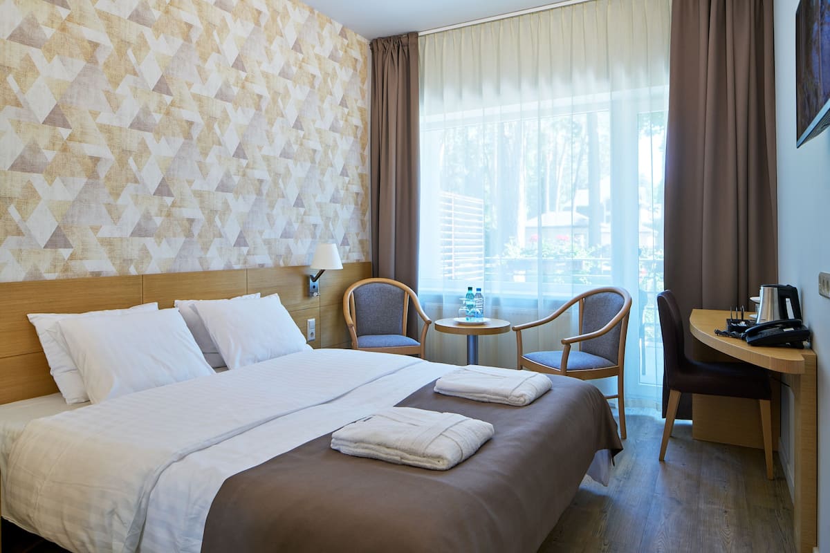 A hotel room with a large bed, two chairs, a small table, and a view of the outdoors.