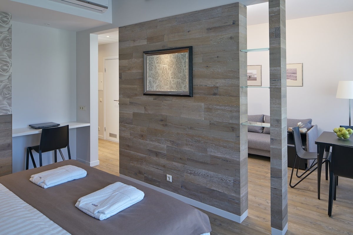 A modern hotel room with a large bed, a desk, a sofa, and a dining area.