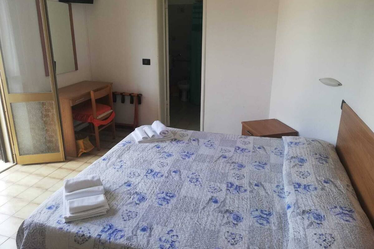 Una habitación de hotel con una cama, un escritorio de madera, una silla, una mesita y un espejo.