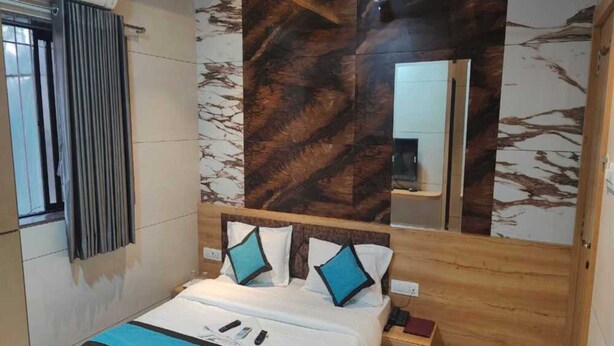A bedroom with a wooden bed, a nightstand, a mirror, and a ceiling fan. - Hotel Prasad NX (Mumbai)