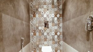A bathroom with a patterned tile wall, a white toilet, and a shower area. - Hotel Prasad NX (Mumbai)