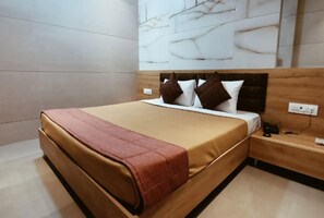 Habitación de hotel moderna con una cama grande, cabecera de madera, pared de mármol y mesita de noche con teléfono y cargador.