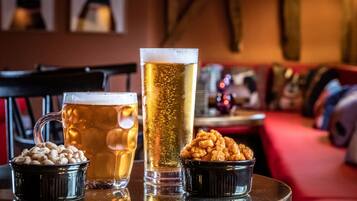 A bar setting with a tall glass of beer, a mug of beer, and two small bowls of snacks on a round table.