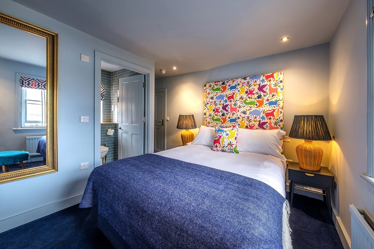 A hotel room with a large bed, a colorful abstract wall art, a mirror, and two bedside lamps.
