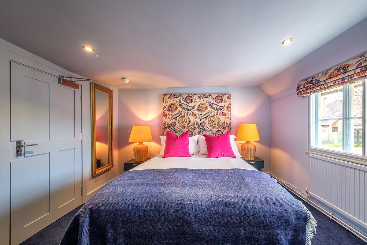 A hotel room with a bed, two bedside lamps, a large mirror, and a window with curtains.