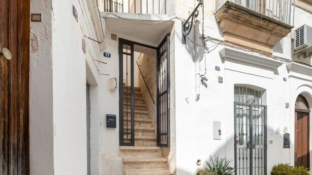 Eine enge Straße mit einem weißen Gebäude, einer Treppe, die zu einer oberen Etage führt, und einem Tor mit einer Nummer.