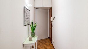 A narrow hallway with a white door, a framed picture on the wall, and a small table with a potted plant. - GuestHost - Apartment located on the first floor of a building without a lift (15 steps at the entrance)In 37 sqm it accommodates 4 people, with a double bedroom and a sofa bed in the living room.Tram stop under the house at 150 meters.Parking on both wh (Padova)