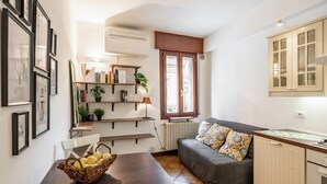 A compact living space with a sofa, a dining table with a basket of fruits, a bookshelf, and a window with a view. - GuestHost - Apartment located on the first floor of a building without a lift (15 steps at the entrance)In 37 sqm it accommodates 4 people, with a double bedroom and a sofa bed in the living room.Tram stop under the house at 150 meters.Parking on both wh (Padova)
