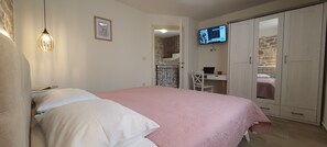 Ein Schlafzimmer mit Bett, Schreibtisch mit Laptop, Fernseher an der Wand und Kleiderschrank.