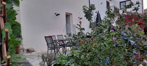Eine Terrasse mit Tisch und Stühlen, umgeben von Pflanzen und Blumen.