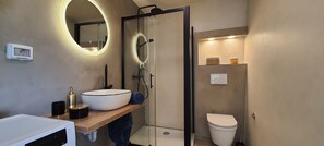 Ein modernes Badezimmer mit rundem Spiegel, Waschbecken in Weiß, einer Duschkabine aus Glas und einer Toilette.