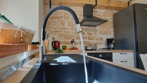 Una cucina con un lavello moderno in acciaio inox, un muro in pietra e un frigorifero nero.
