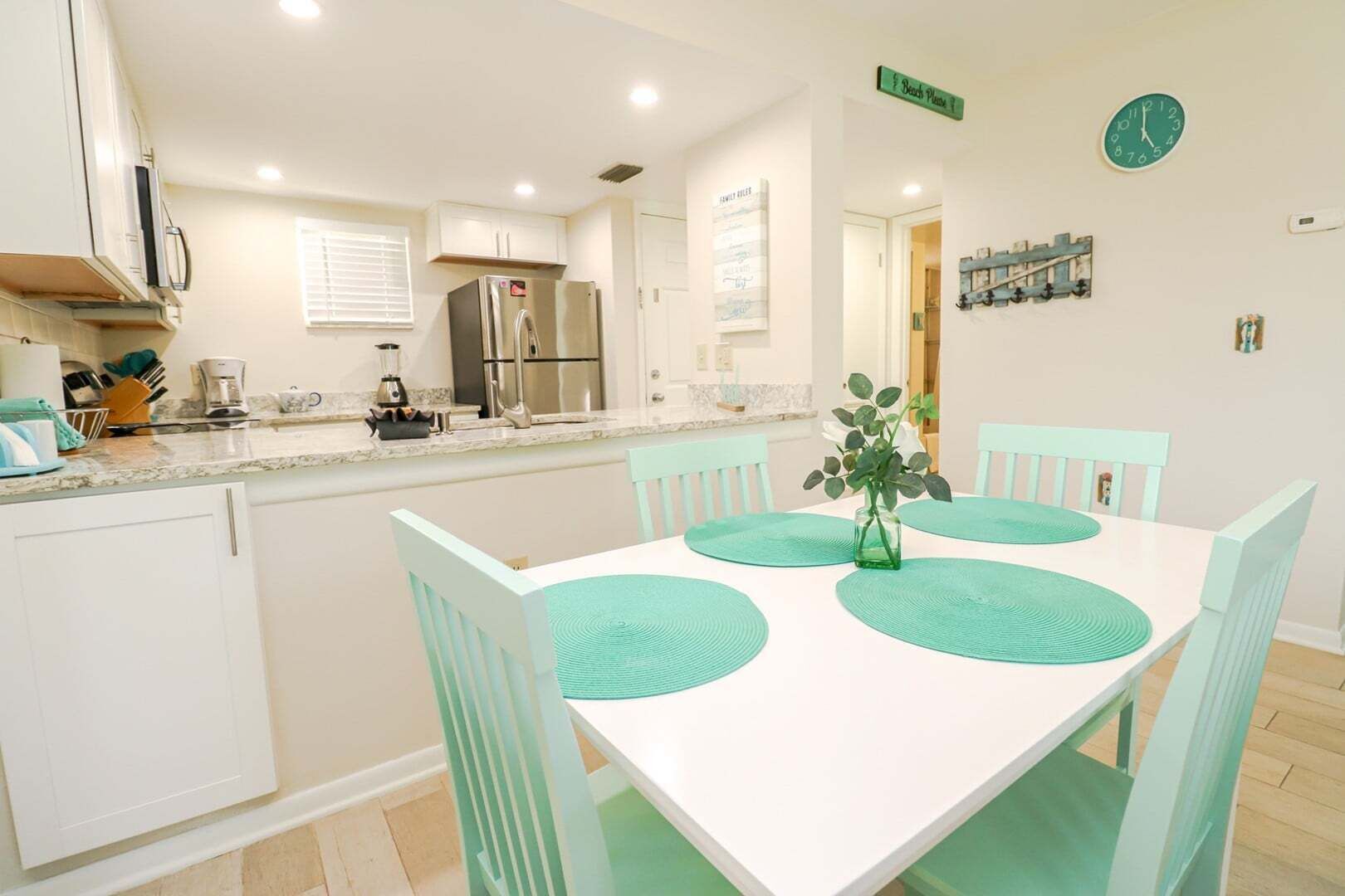 A modern kitchen with white cabinets, stainless steel appliances, and a dining area with a white table and turquoise chairs.