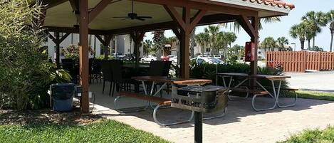 An outdoor patio area with tables and chairs, a trash can, and a covered seating area.