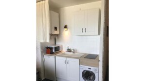 A compact kitchen with white cabinets, a microwave, a sink, and a washing machine. - Studio au Pied de la Plage (Canet-en-Roussillon)