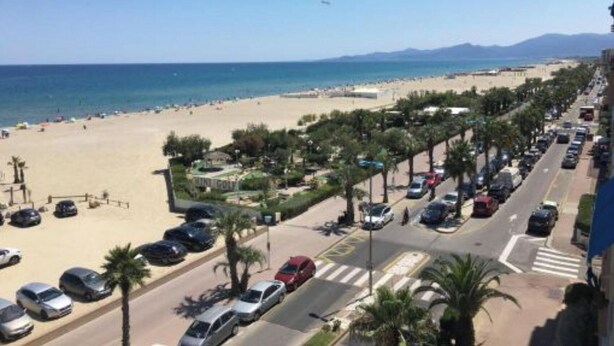 A beachside road with parked cars, a pedestrian crossing, and a clear view of the beach and ocean. - Studio au Pied de la Plage (Canet-en-Roussillon)