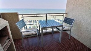 A balcony with a table and two chairs, overlooking a beach with visible cars and buildings. - Studio au Pied de la Plage (Canet-en-Roussillon)