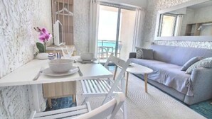 A modern room with a white dining table, chairs, a sofa, and a small round table. - Studio au Pied de la Plage (Canet-en-Roussillon)