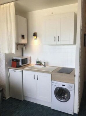 A compact kitchen with white cabinets, a microwave, a sink, and a washing machine.