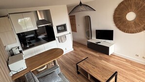 Een moderne woonkamer met een bank, een houten salontafel, een televisie en een keukenhoek met een magnetron.