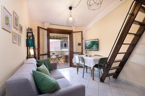 Un salon avec un canapé, une table à manger et un téléviseur. On peut voir un escalier et un balcon.