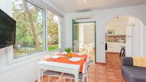 Un comedor con una mesa lista para cuatro personas, un televisor montado en la pared y vistas al exterior.