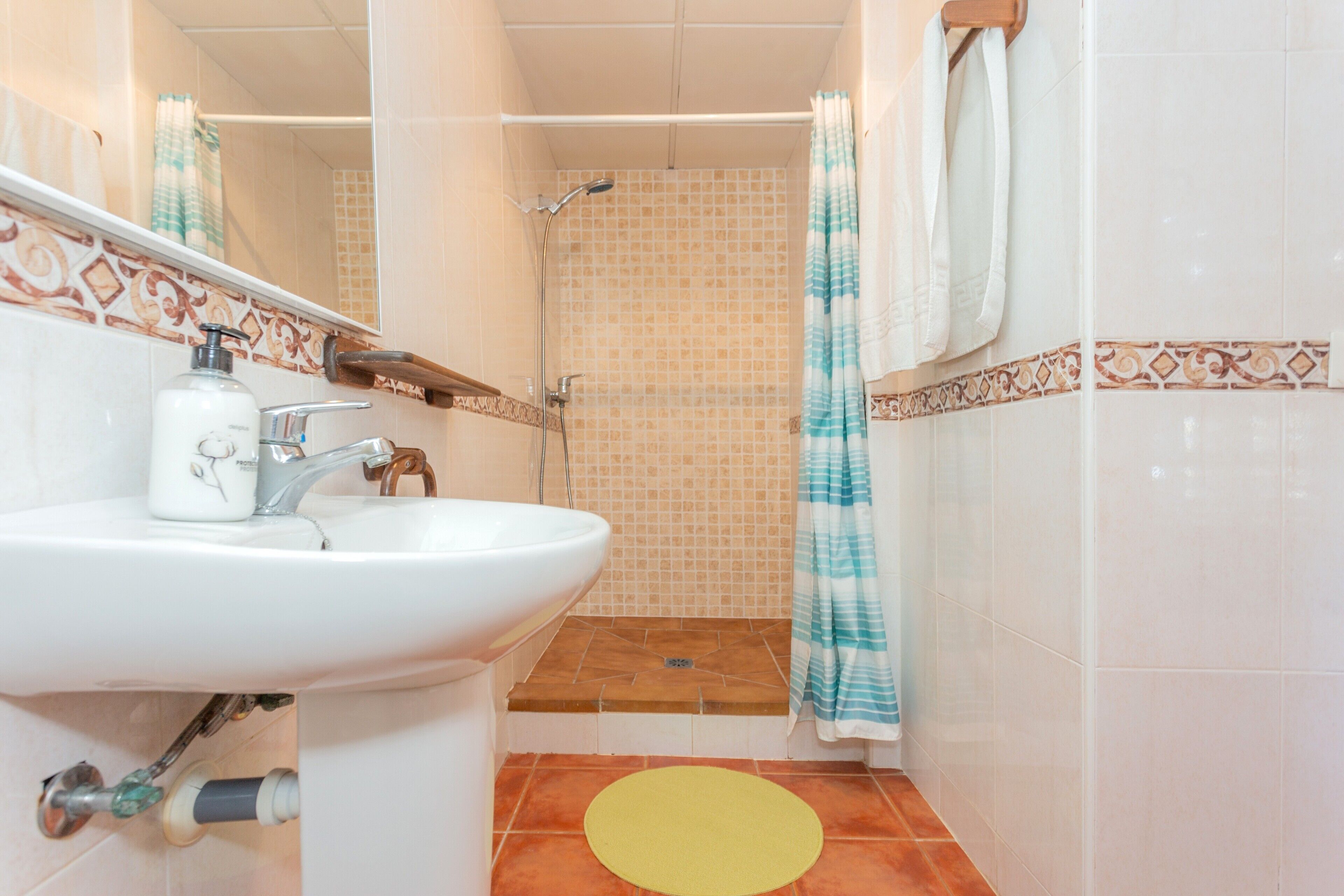 Un baño con lavamanos, ducha y un tapete amarillo.