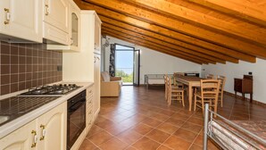 Une cuisine équipée d’une cuisinière, d’un four et de placards, un coin repas avec une table et des chaises, et un plafond en bois particulièrement haut.