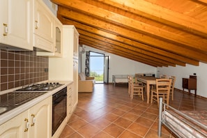 A kitchen with a stove, oven, and cabinets, a dining area with a table and chairs, and a high wooden ceiling.