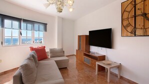 Una sala de estar con un sofá modular, un televisor, un mueble de madera y un reloj en la pared.