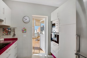 A kitchen with white cabinets, a stainless steel refrigerator, and a clock on the wall.