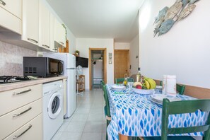 A compact kitchen with a microwave, washing machine, and a dining area with a table set for two.
