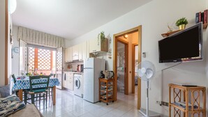 A compact living space with a dining area, kitchen, and a TV mounted on the wall. - Holiday Home 'L'Acquario' with Mountain View, Terrace & A/C (Villasimius)