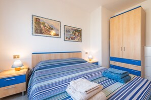 A bedroom with a bed, two paintings, a wardrobe, a nightstand with a lamp, and a bedside table.