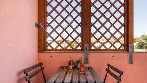 A wooden table with two bottles and two chairs in a room with a lattice window and a pink wall. - Holiday Home 'L'Acquario' with Mountain View, Terrace & A/C (Villasimius)
