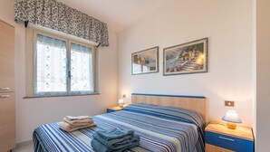 A bedroom with a bed, two bedside tables, a nightstand, a window with curtains, and two wall-mounted paintings. - Holiday Home 'L'Acquario' with Mountain View, Terrace & A/C (Villasimius)