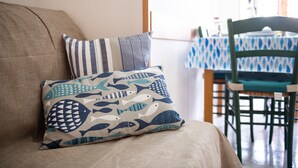 A sofa with patterned cushions, a dining table with a blue and white tablecloth, and a chair with a green frame. - Holiday Home 'L'Acquario' with Mountain View, Terrace & A/C (Villasimius)