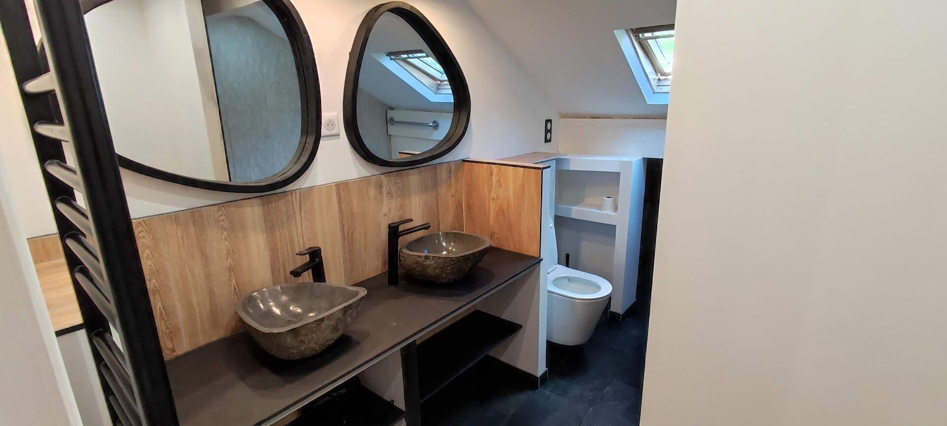Een moderne badkamer met twee wasbakken van natuursteen, een wit toilet en een dakraam.