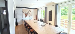 Una cocina moderna con una larga mesa de comedor, sillas, un adorno en la pared y vistas a la vegetación a través de amplios ventanales.