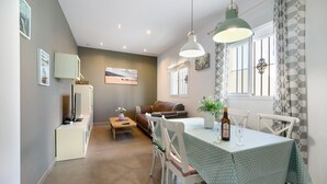 A dining area with a table, chairs, a hanging light fixture, a window with curtains, and a sofa in the background. - Pet-Friendly Piso Arquillo del Reloj Apartment with Wi-Fi (Chiclana de la frontera)