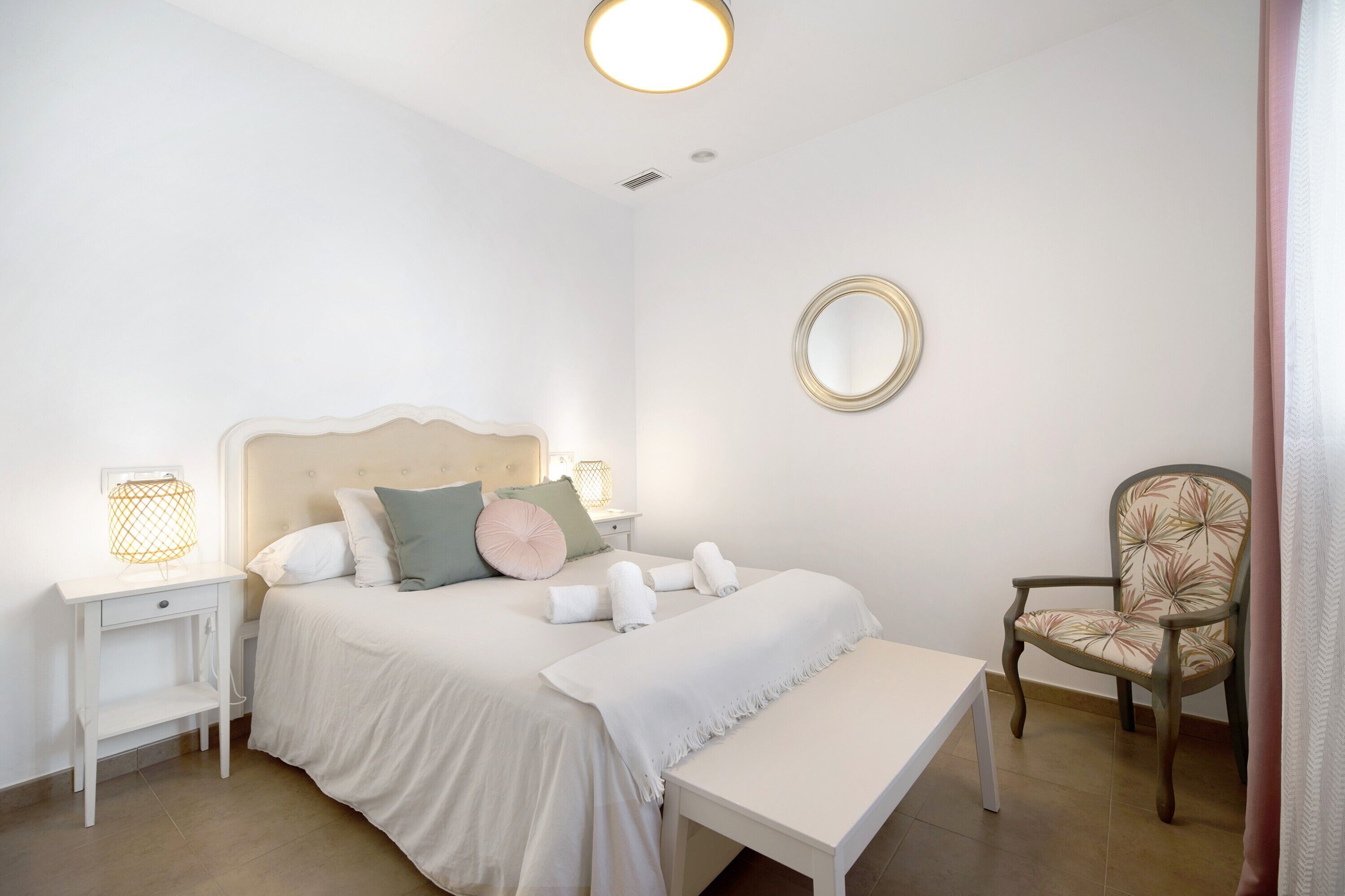 Een slaapkamer met een bed, nachtkastjes, een stoel, een spiegel en een bankje.