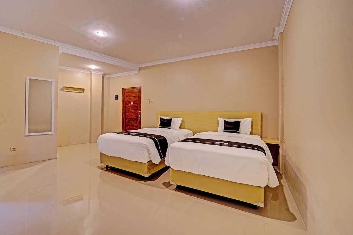 A hotel room with two beds, a mirror, a door, and a light fixture.