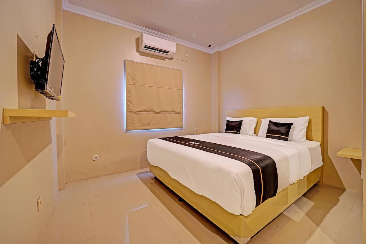 A neatly arranged bedroom with a bed, a window with blinds, an air conditioning unit, and a shelf with a decorative item.