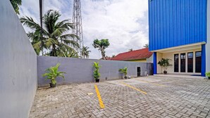 A paved courtyard with potted plants, a blue building, and a palm tree. - Super OYO Collection O Andono Hotel (Temon)