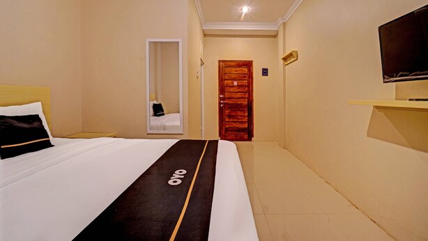 A hotel room with a bed, a television on a stand, a mirror, and a door. - Super OYO Collection O Andono Hotel (Temon)