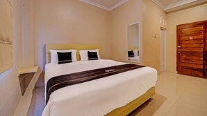 A hotel room with a large bed, a wooden door, and a mirror on the wall. - Super OYO Collection O Andono Hotel (Temon)