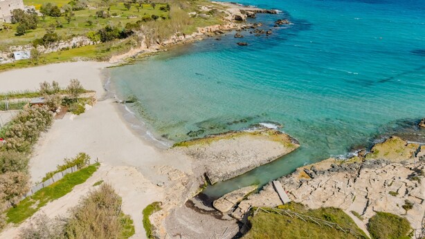 Luftaufnahme einer Küstenlandschaft mit Strand, felsigem Ufer und Wohngebäuden.